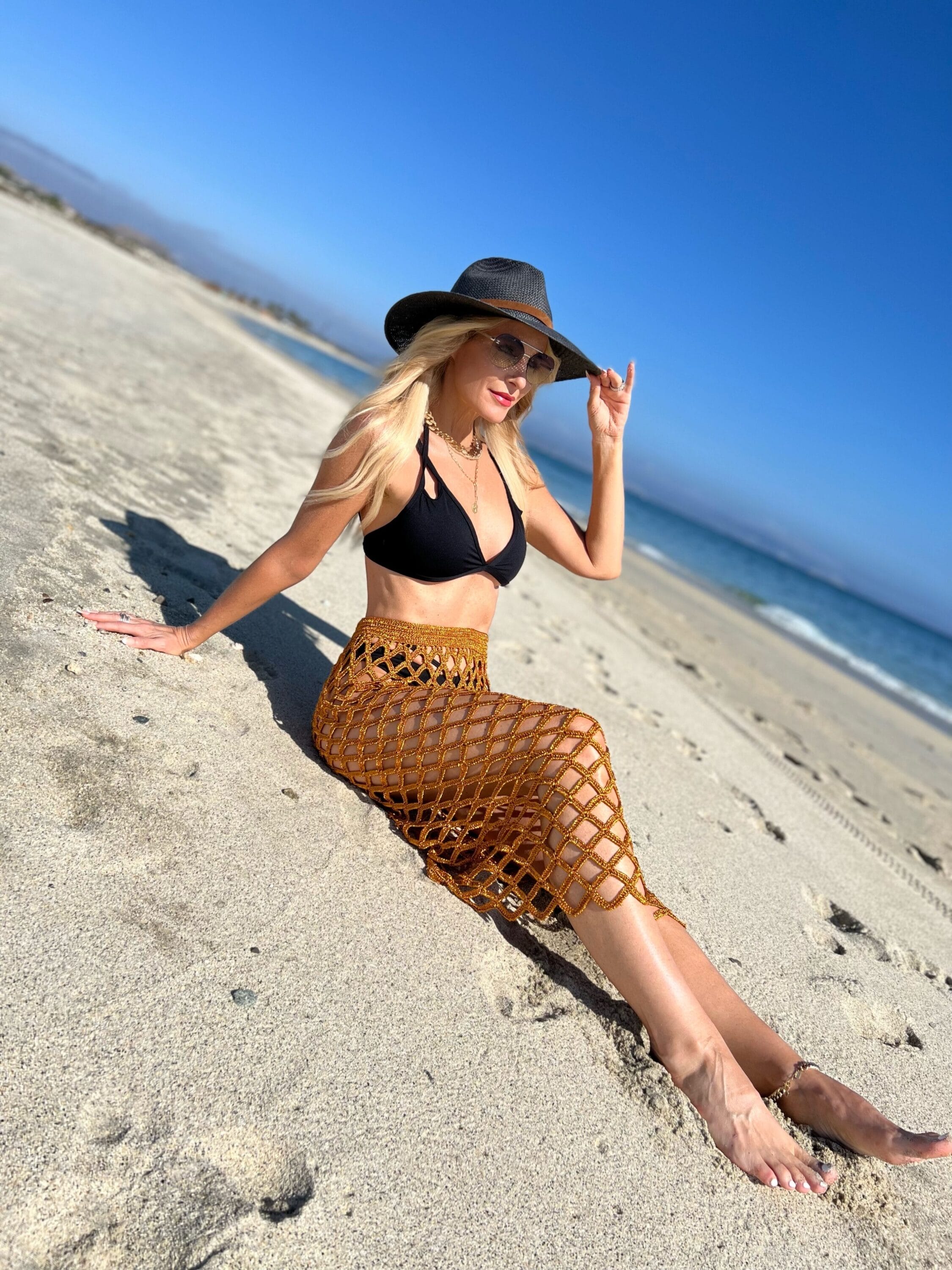 Dallas fashion blogger over 40 wearing black bikini and crochet cover up laying on sandy beach