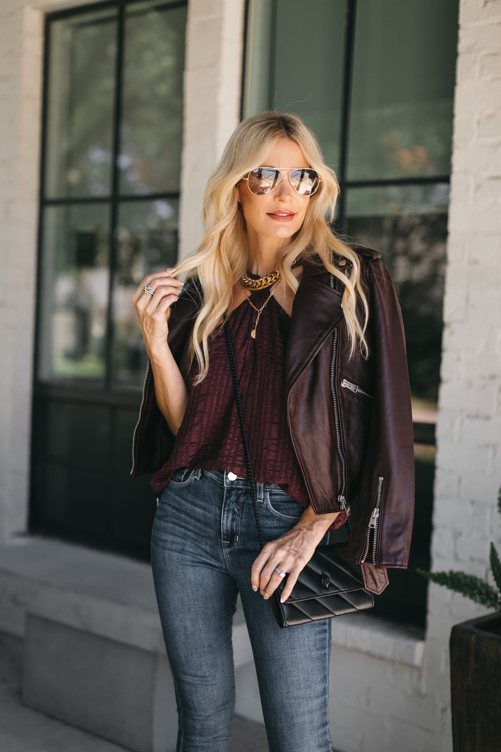 Fashion blogger over 40 wearing leather jacket with flare jeans and drape top