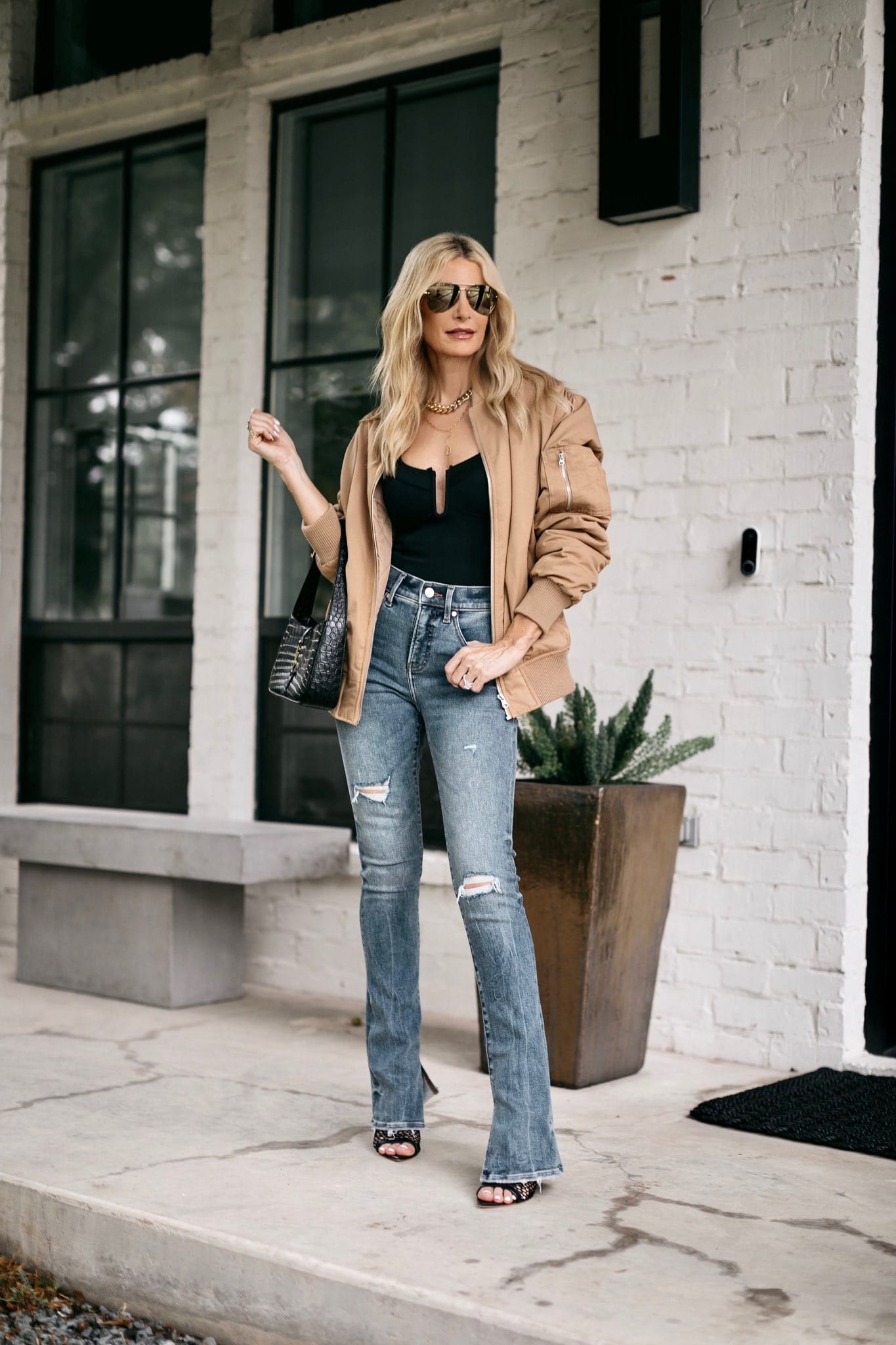 fashion blogger over 40 wearing oversize bomber jacket with ripped flares and black bodysuit.