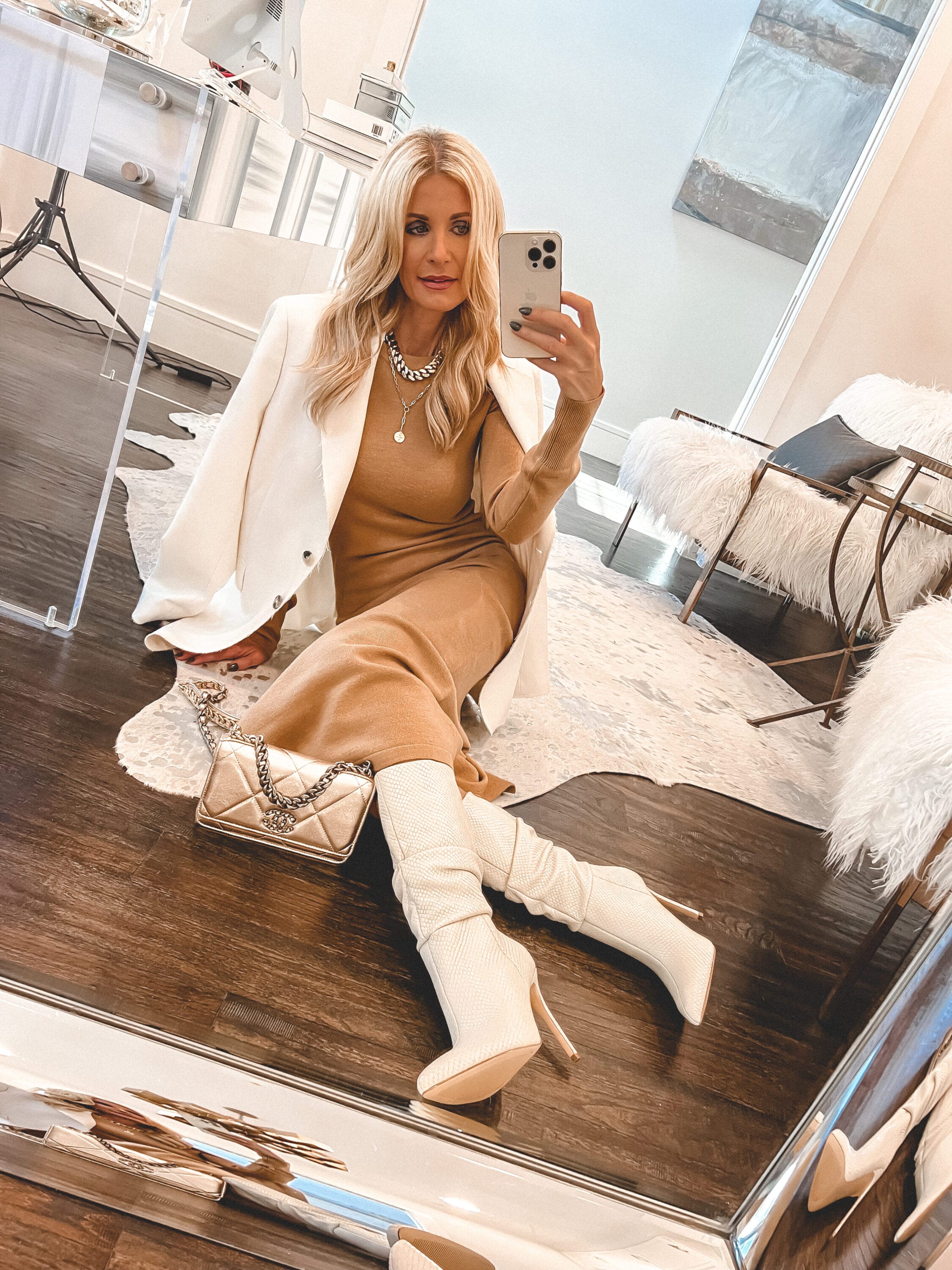 Over 40 woman wearing camel sweater dress with oversized white blazer and ivory slouch boots.