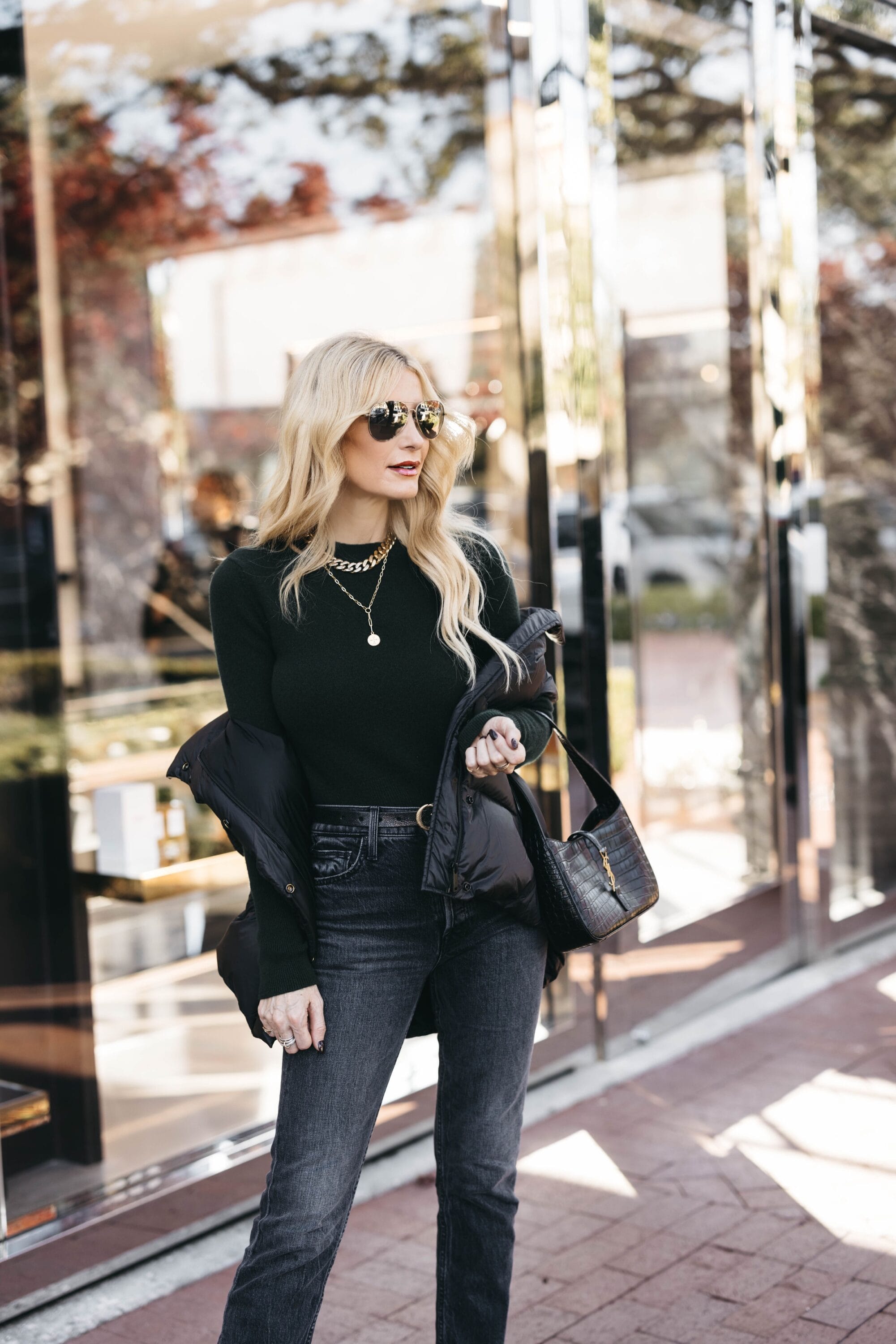 fashionista over 40 wearing black puffer vest with black longsleeve bodysuit and vintage black jeans.
