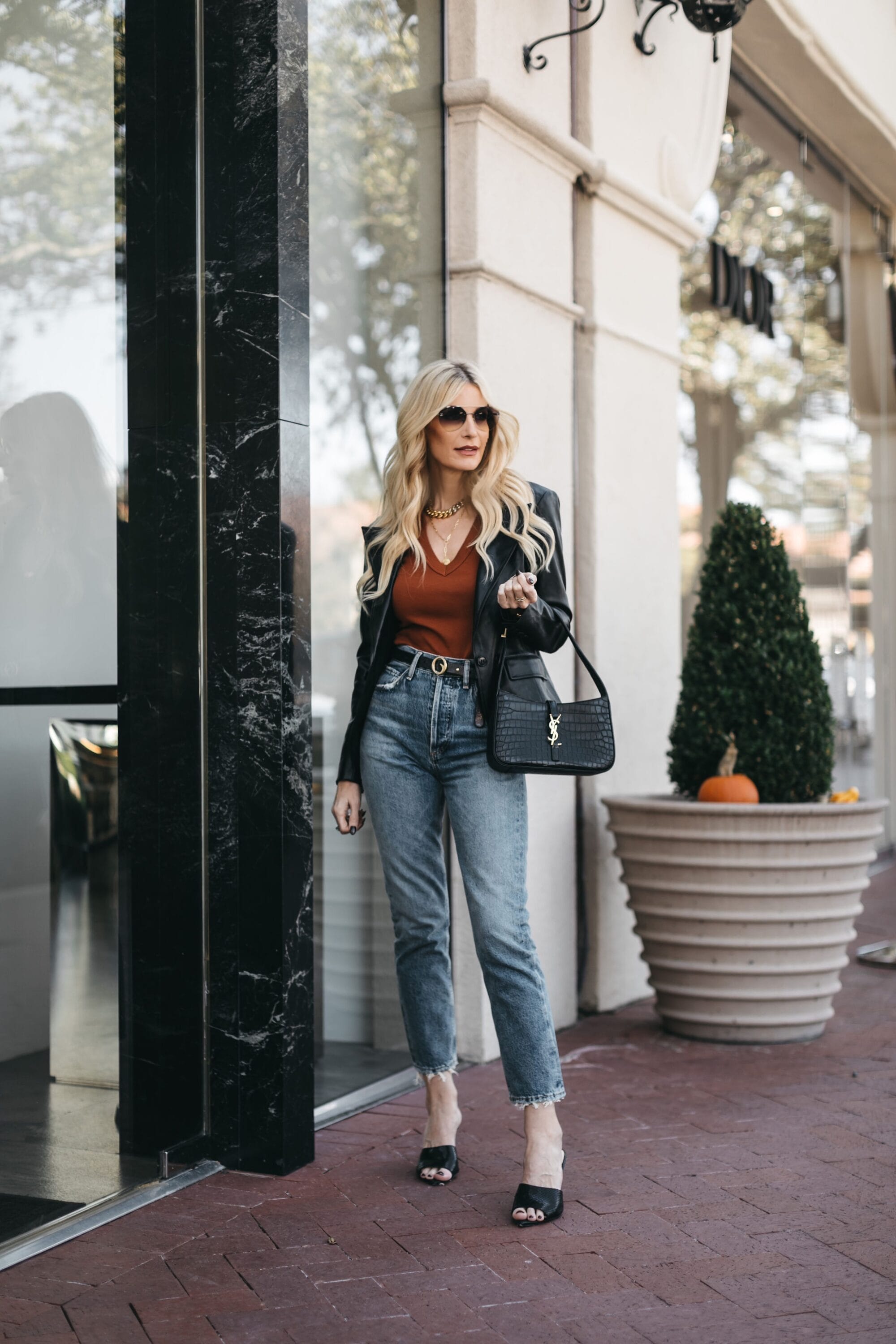 Over 40 fashion influencer modeling agolde riley jeans with rust t-shirt and black jacket with pointed toe black sandals.
