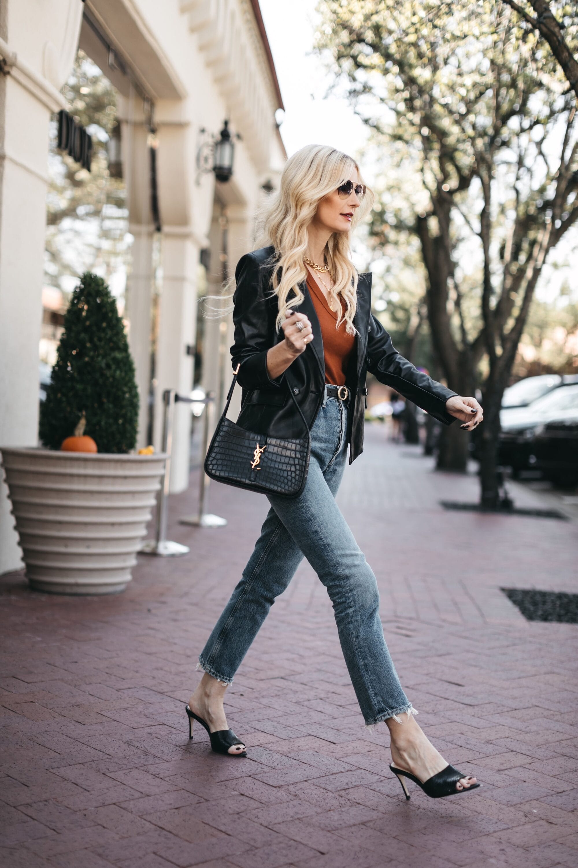 Over 40 fashion influencer wearing black heeled sandals with cropped riley jeans and rust colored top underneath black faux leather blazer from Evereve.