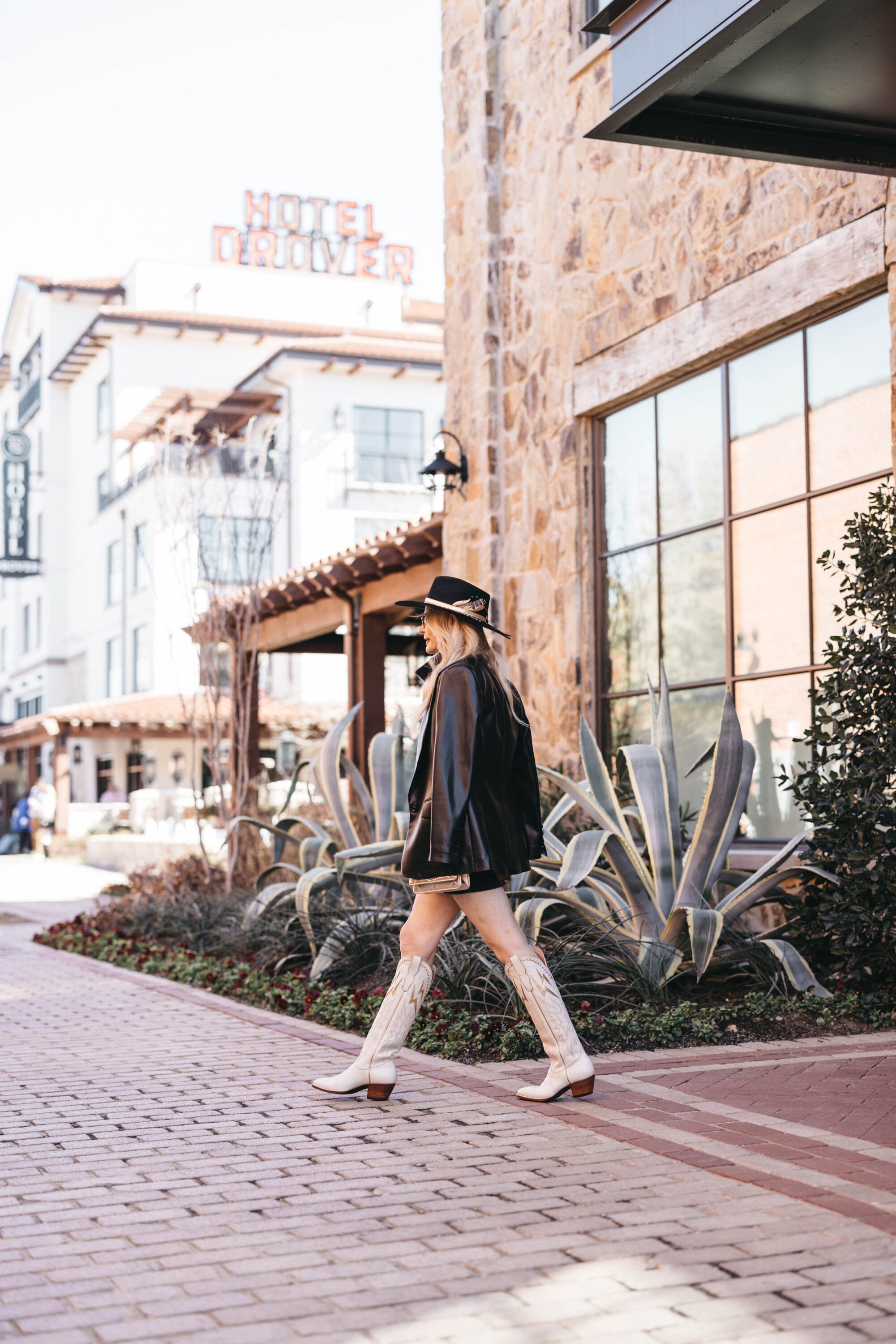 Over 40 fashion blogger wearing her western best including a black denim dress with a vegan leather blazer and City boots cowboy boots in front of Hotel Drover.