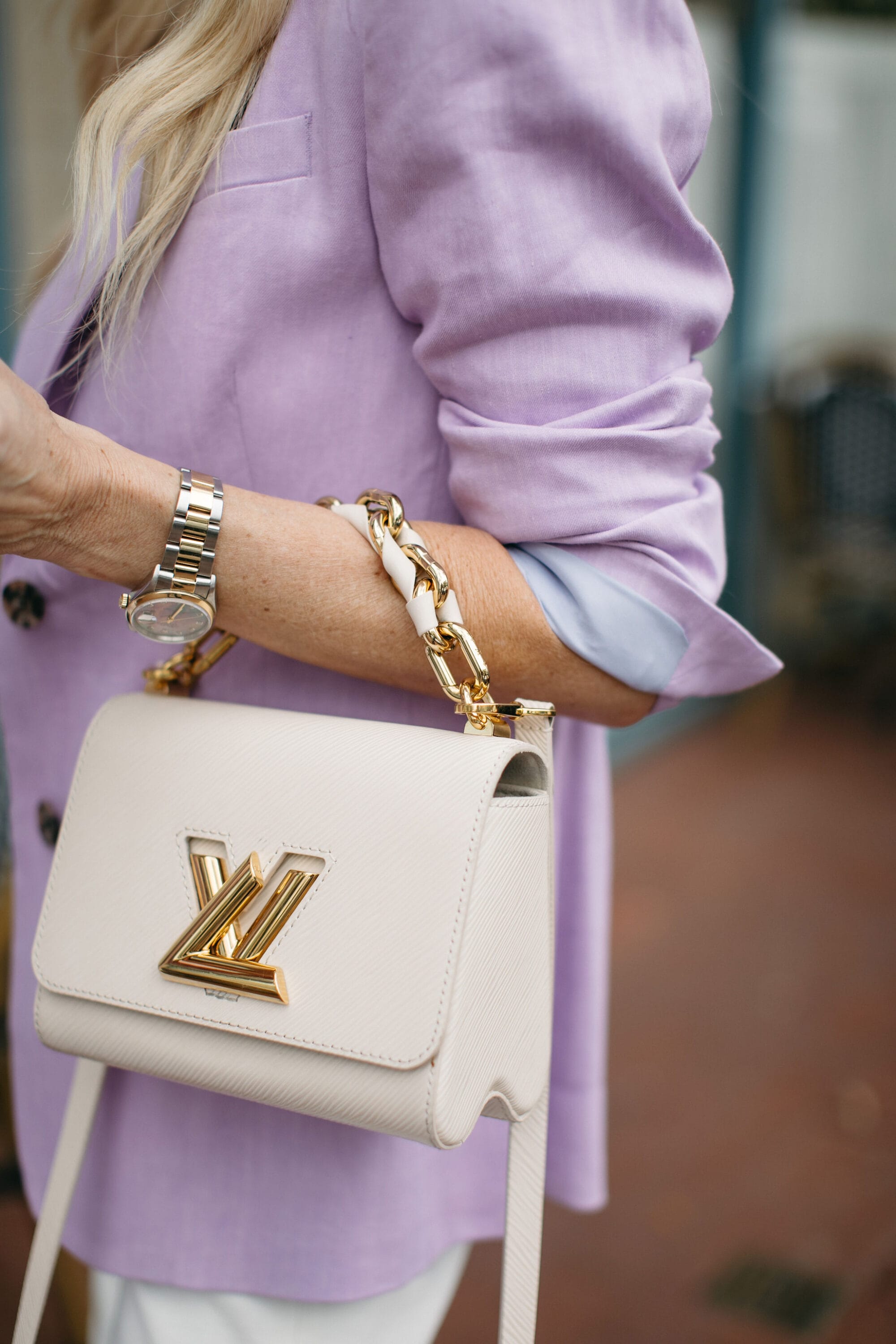Style shot of a white & gold Louis Vitton handbag paired with a lavender blazer and white denim.
