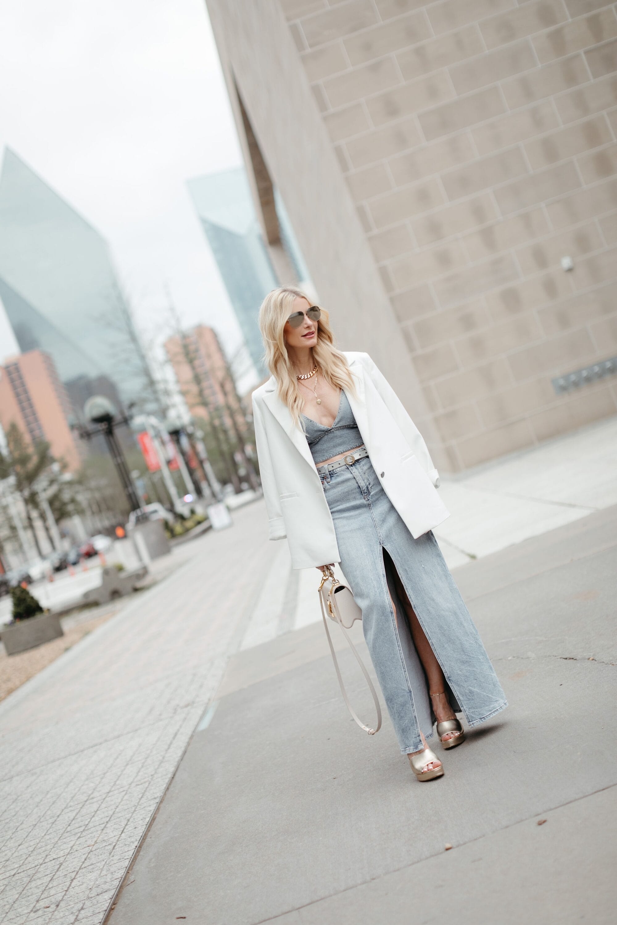 Dallas fashion writer for the over 40 niches wearing a crop bra top with a white blazer draped over top paired with a denim midi skirt.