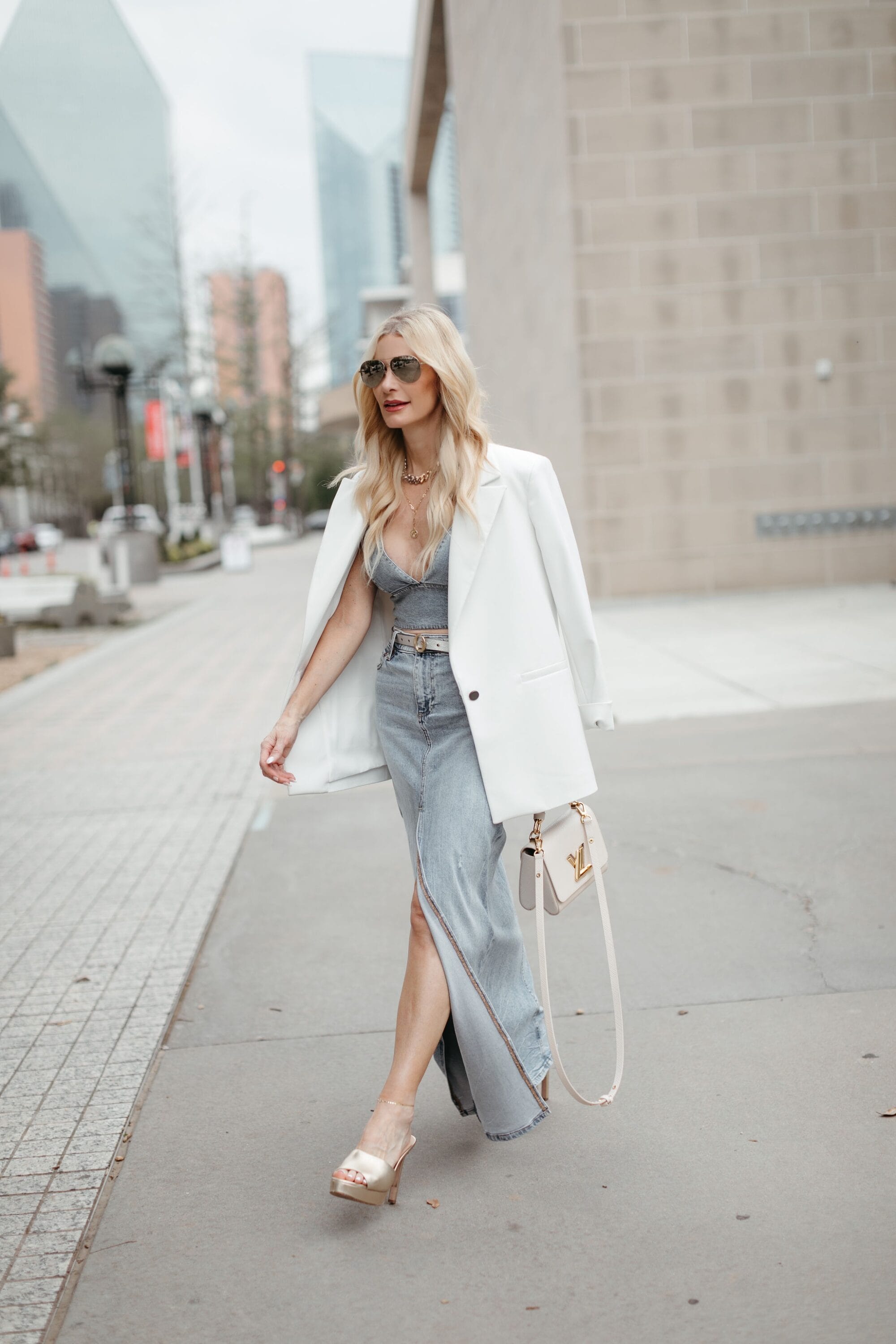 Over 40 woman wearing denim bra top with white blazer and maxi skirt.