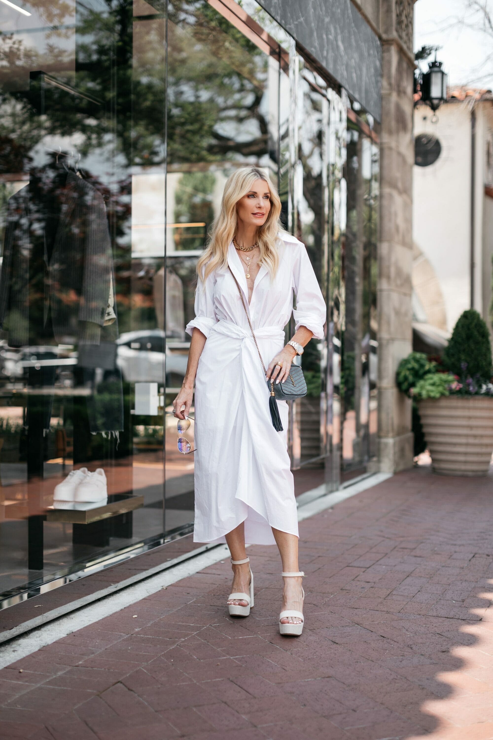 Over 40 fashion blogger wearing a white dress tied at the waist with white platforms as an example of how to look slimmer in a dress.