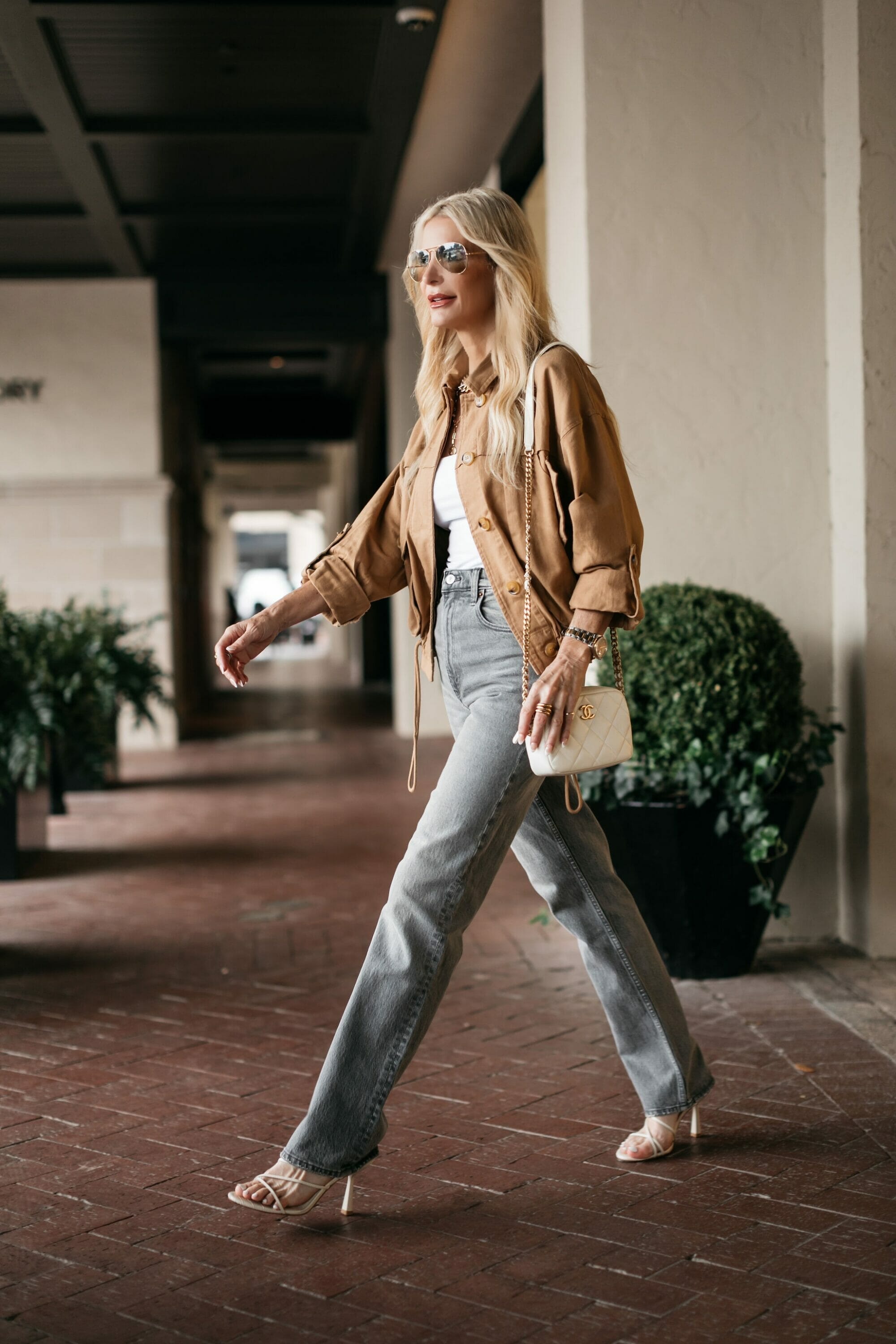 woman over 40 wearing camel jacket with gray jeans and a white bodysuit.