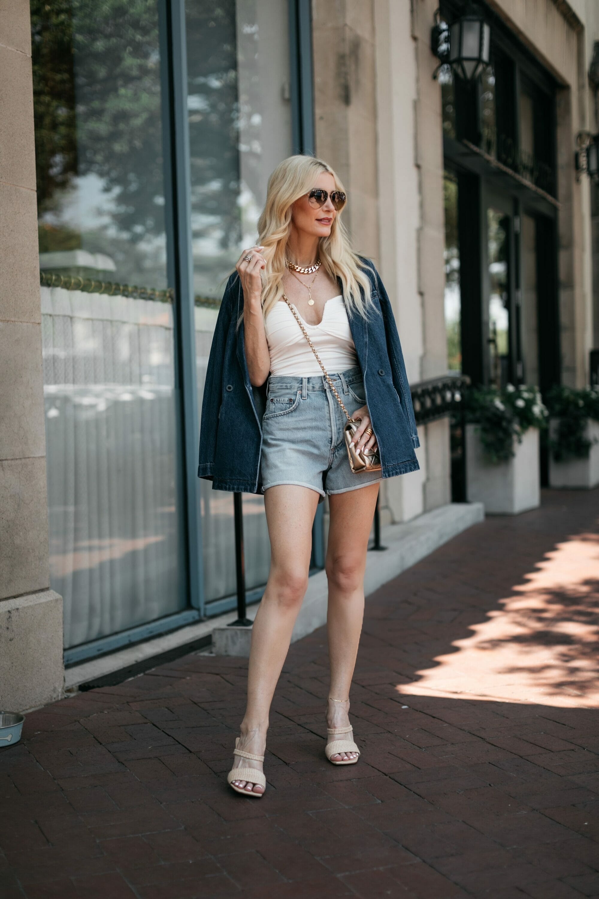 Dallas woman over 40 wearing Agolde shorts with a white strapless top and a denim blazer as one of the best transitional jackets.